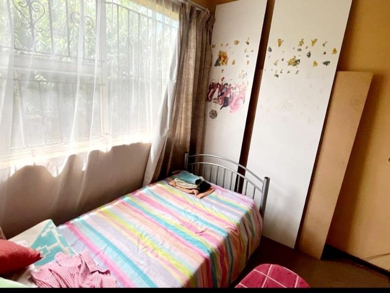 A bedroom featuring a window with security bars and plain wall finishes, requiring cosmetic updates to improve the overall condition.