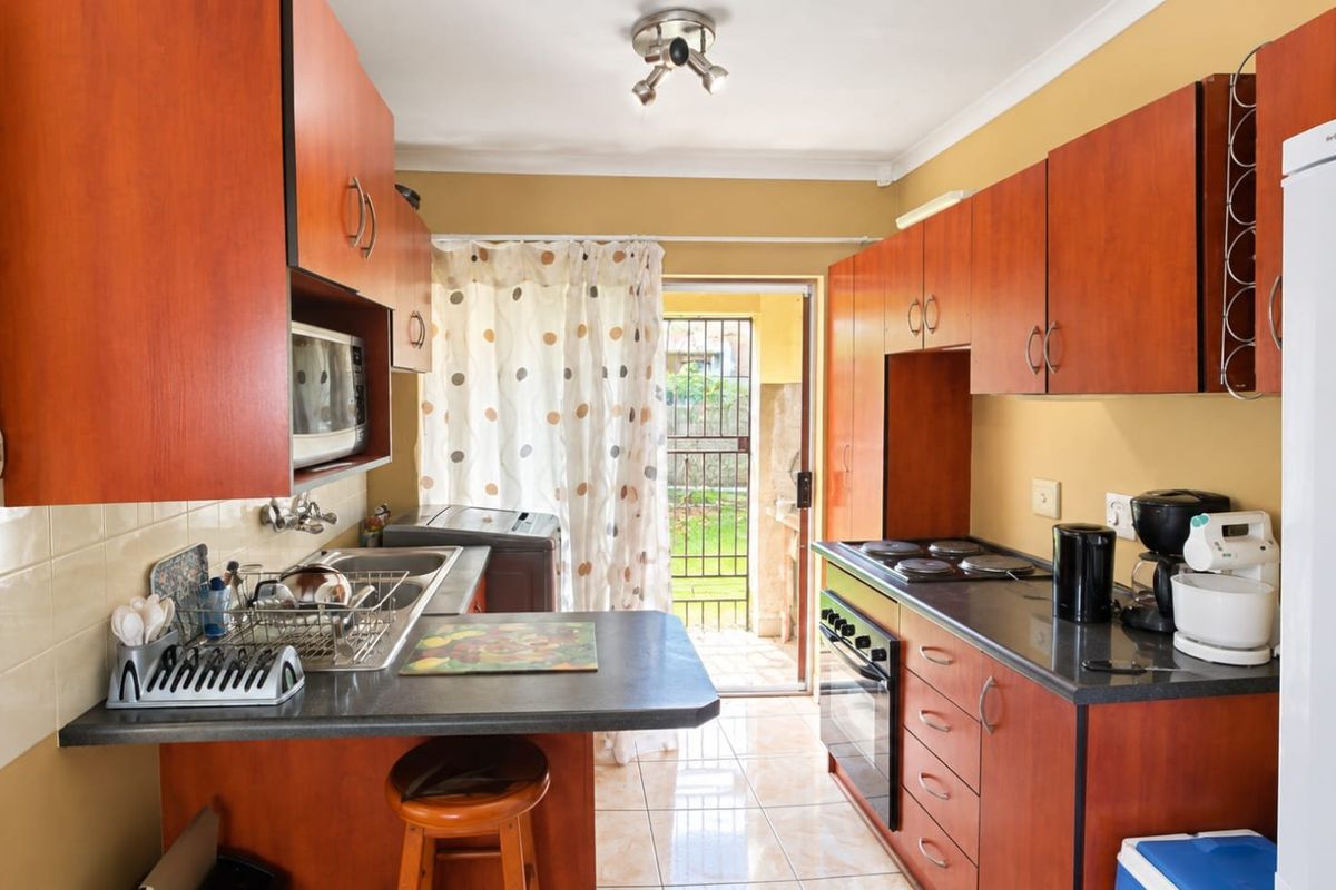 Functional kitchen featuring wood-finish cabinetry, dark laminate countertops, built-in oven and hob, and direct access to the rear garden area.