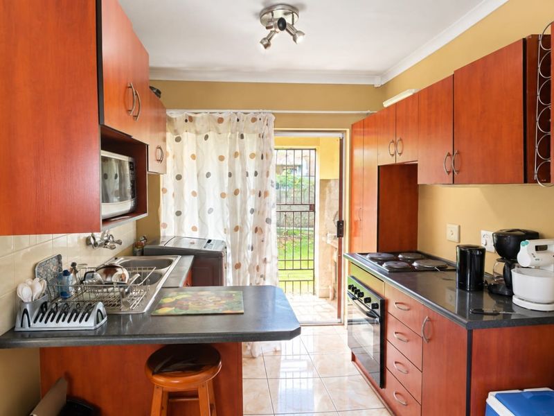 Functional kitchen featuring wood-finish cabinetry, dark laminate countertops, built-in oven and hob, and direct access to the rear garden area.