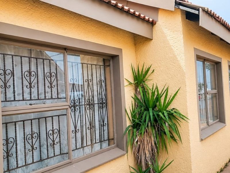A side view of the property featuring a yellow stucco facade, security bars on the windows, and a paved walkway.