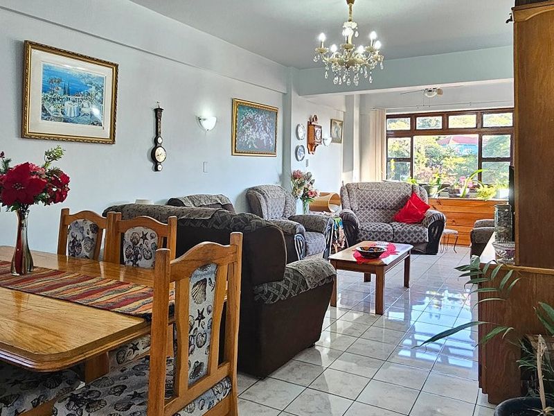Spacious open-plan living and dining area featuring tiled flooring, a classic chandelier, and large windows providing natural light.