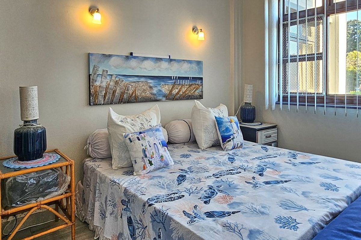 A well-maintained bedroom featuring wall-mounted lighting, a window with security bars, and vertical blinds, offering a comfortable and functional living space.