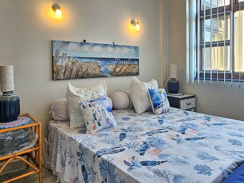 A well-maintained bedroom featuring wall-mounted lighting, a window with security bars, and vertical blinds, offering a comfortable and functional living space.