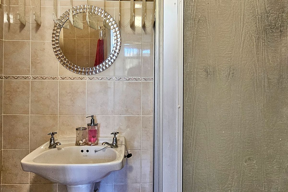 A functional bathroom featuring a pedestal basin, tiled walls, and a shower enclosure with a sliding door.