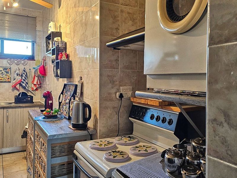 A functional kitchen featuring tiled walls and flooring, built-in cabinetry, a stainless steel sink, and a freestanding stove with an extractor fan.