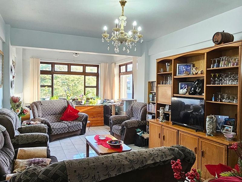 A spacious living room featuring tiled flooring, a decorative chandelier, and large windows that provide ample natural light.