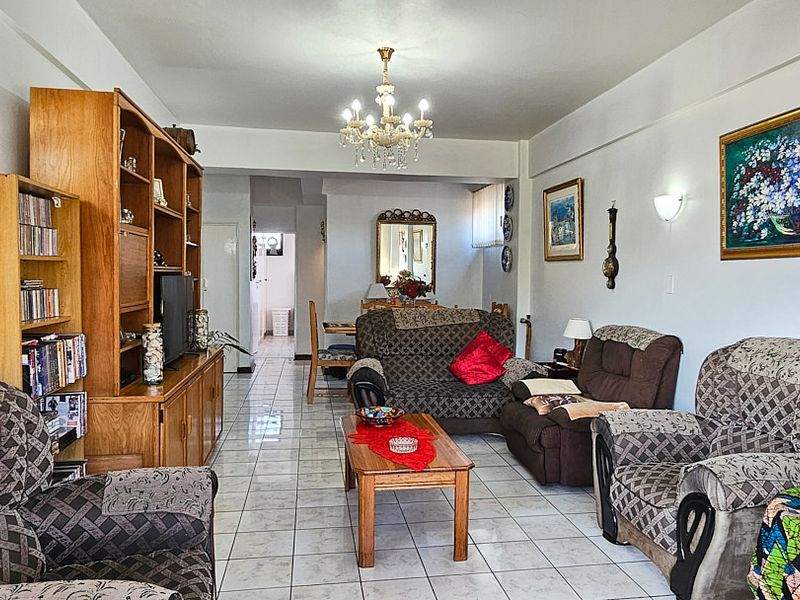 A spacious living room featuring light-colored tiled flooring and a decorative crystal chandelier, offering a functional layout for comfortable family living.