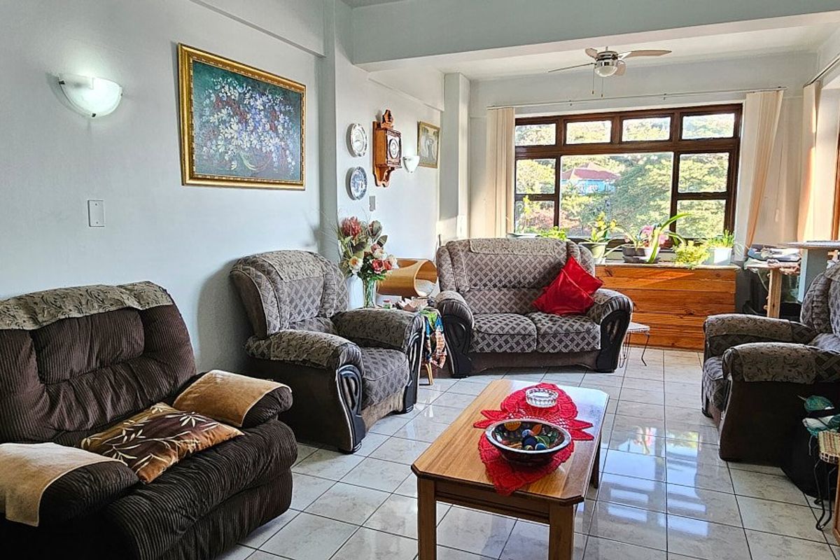 A spacious living room featuring tiled flooring, a ceiling fan, and large windows that provide ample natural light and views.