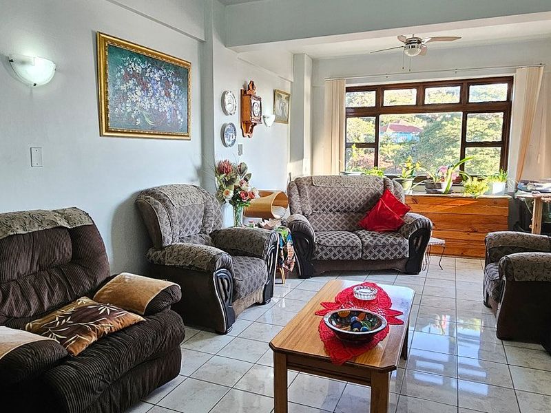 A spacious living room featuring tiled flooring, a ceiling fan, and large windows that provide ample natural light and views.