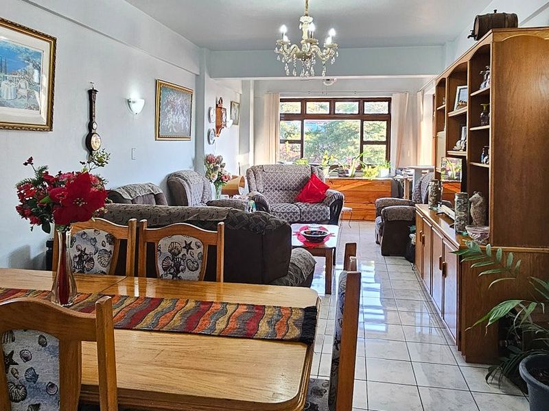 Spacious open-plan living and dining area featuring tiled flooring, a central chandelier, and large windows providing natural light.