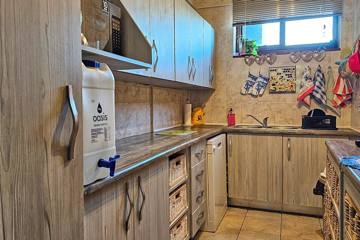 A functional kitchen featuring wood-look laminate cabinetry, tiled backsplash, and durable tiled flooring with ample storage space.