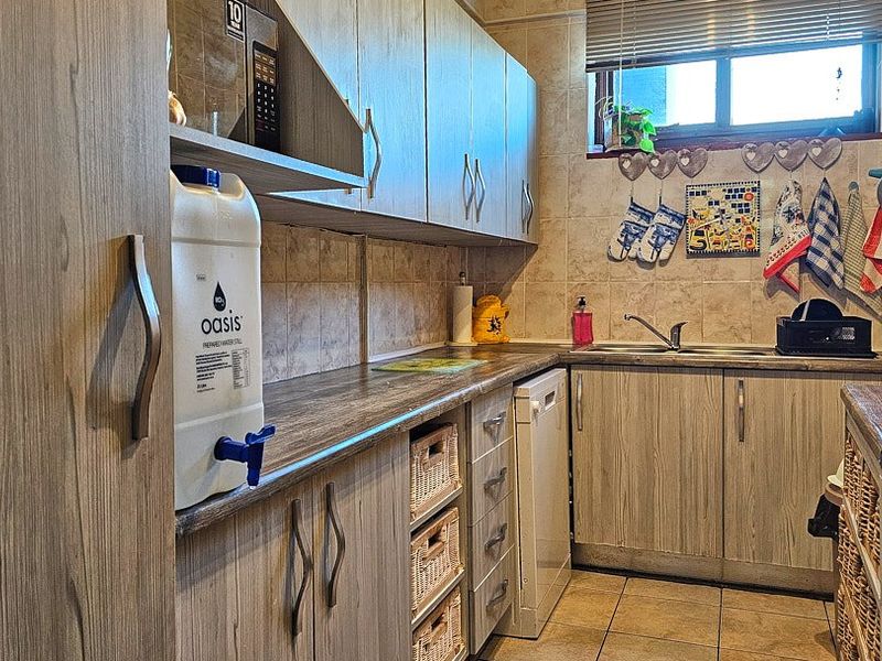 A functional kitchen featuring wood-look laminate cabinetry, tiled backsplash, and durable tiled flooring with ample storage space.