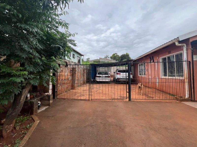 Front exterior view of the property featuring a paved driveway, metal security gate, and a covered carport area.