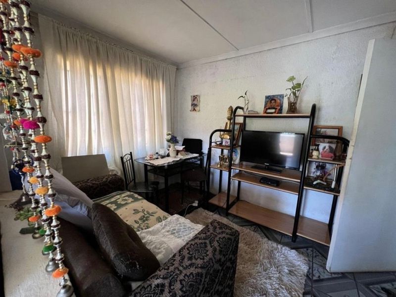 A compact living room featuring tiled flooring and large windows with curtains, requiring cosmetic updates to the walls and ceiling.