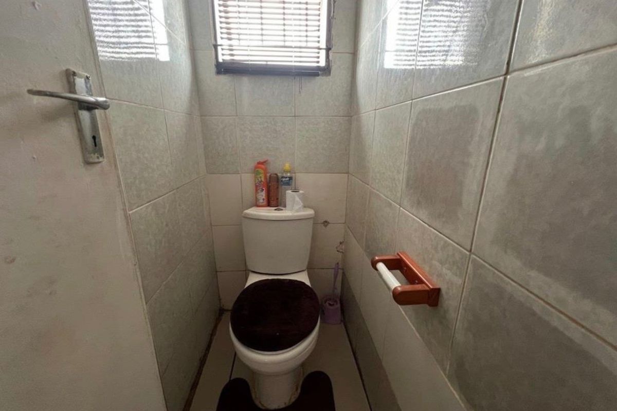 A compact bathroom featuring tiled walls and flooring, equipped with a standard toilet and a window with fitted blinds.