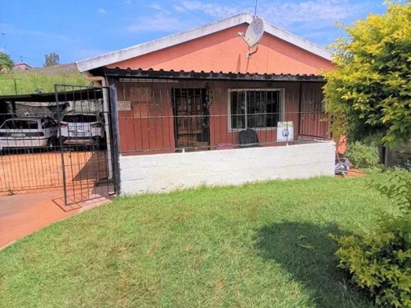 Front view of a detached residential property featuring a small front garden, security bars, and an attached carport area.