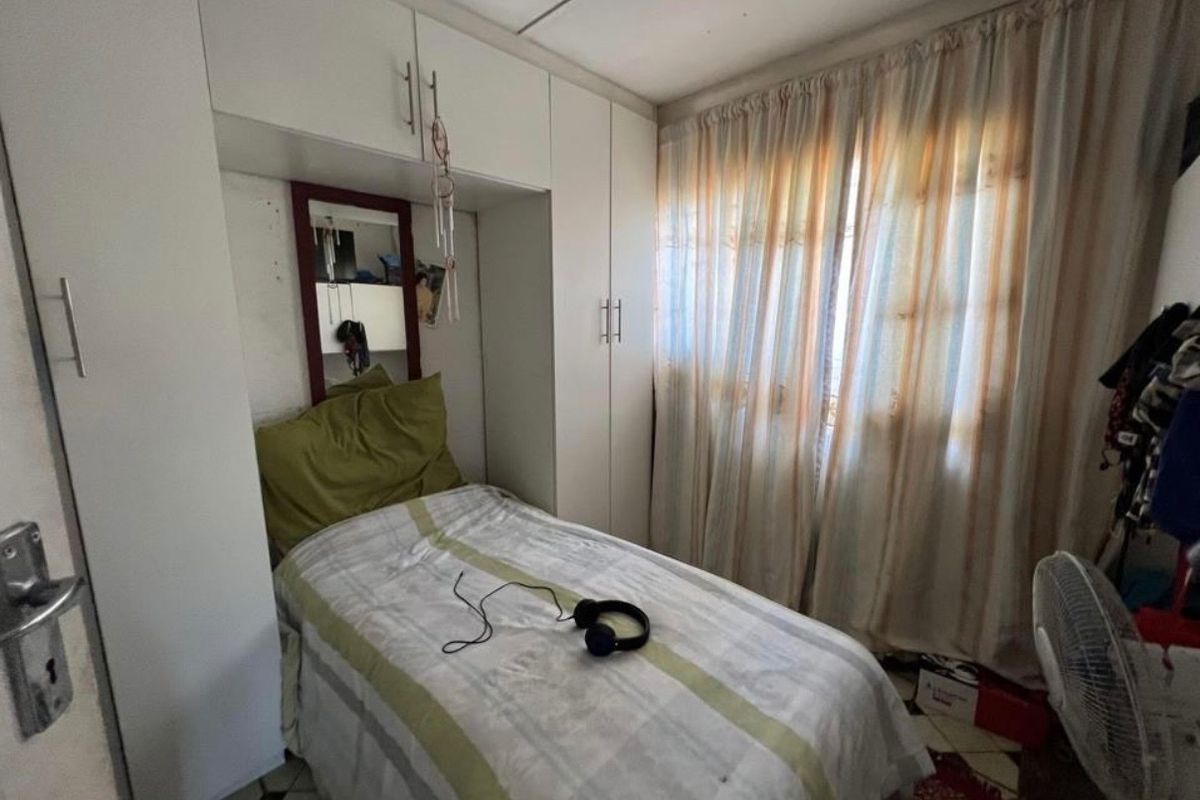 A compact bedroom featuring built-in cupboards and overhead storage units, providing efficient use of space with natural light from the window.