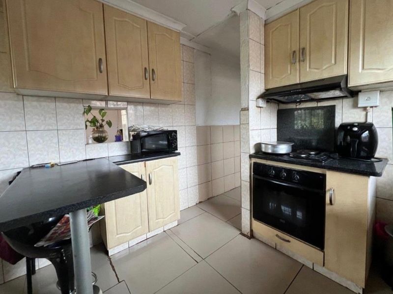 A functional kitchen featuring built-in cabinetry, a gas hob with extractor, and a breakfast bar, offering potential for modernization.