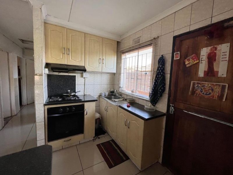 Compact kitchen featuring built-in cabinetry, gas hob, oven, extractor fan, and tiled finishes. Requires cosmetic updates to modernize the space.
