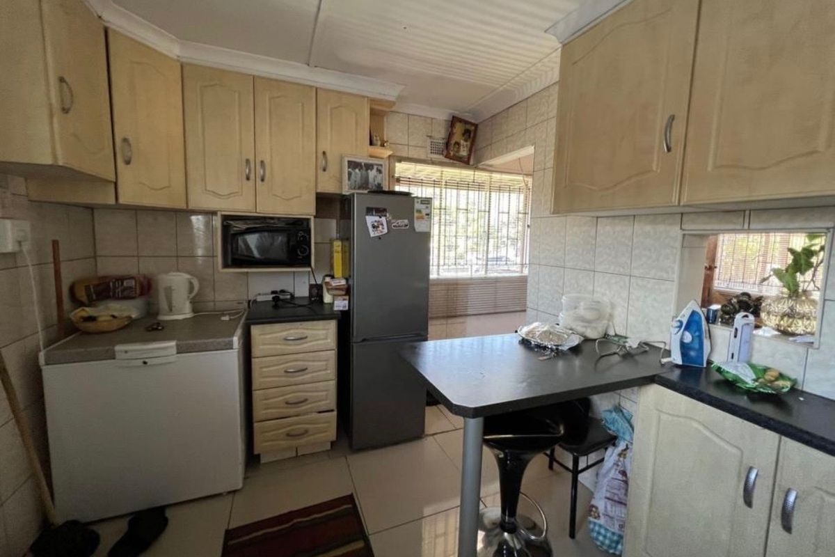 A functional kitchen featuring built-in cabinetry, tiled backsplash, and tiled flooring, offering a practical layout with integrated appliance space and security window bars.