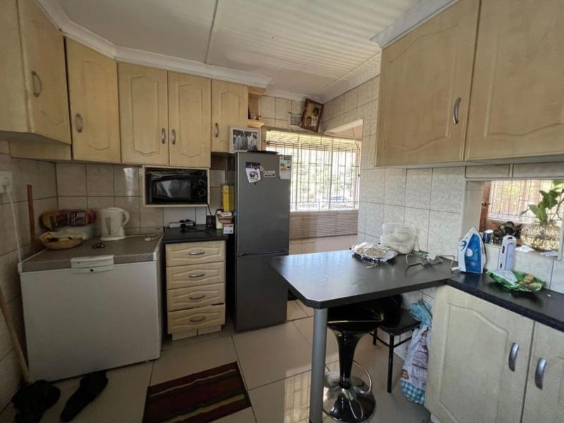 A functional kitchen featuring built-in cabinetry, tiled backsplash, and tiled flooring, offering a practical layout with integrated appliance space and security window bars.