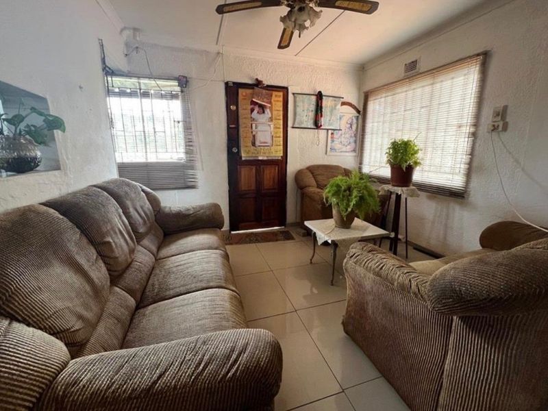 A living room featuring tiled flooring, a ceiling fan, and security features, requiring cosmetic updates to improve the overall aesthetic and finish.