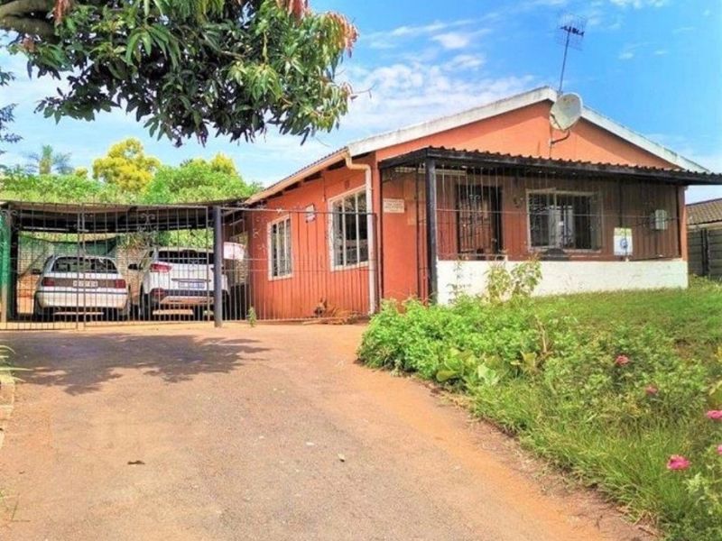 Front exterior view of a single-story residential property featuring a paved driveway, attached carport, and security fencing.