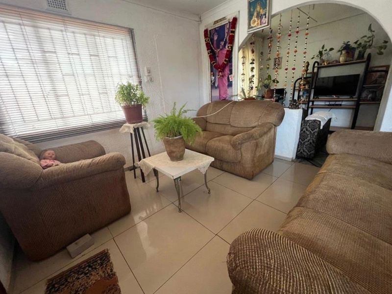A living room featuring tiled flooring, an arched doorway leading to an adjacent space, and large windows fitted with venetian blinds.