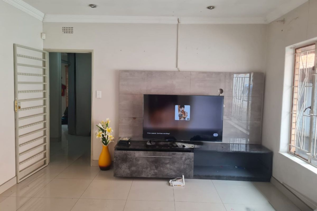 Living room featuring a built-in media unit, tiled flooring, and security features including a gate and burglar bars.