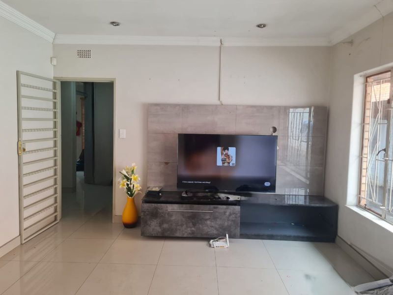 Living room featuring a built-in media unit, tiled flooring, and security features including a gate and burglar bars.