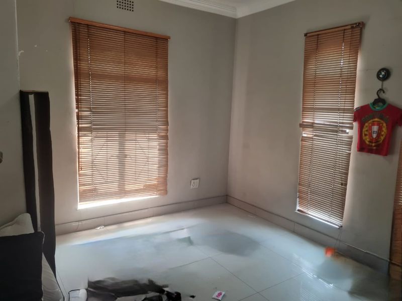 A vacant bedroom featuring tiled flooring and dual windows fitted with wooden venetian blinds.