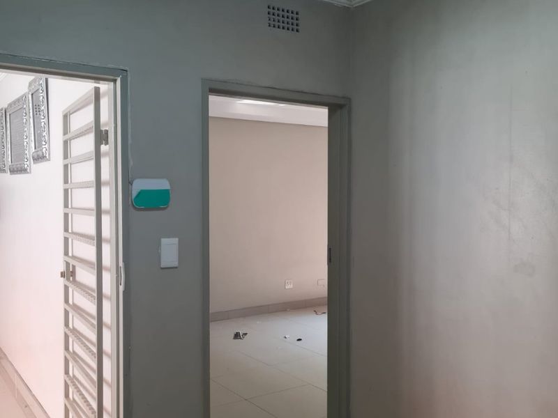 A neutral hallway featuring tiled flooring, a security gate, and access to an adjacent room, presenting a clean and functional transition space.