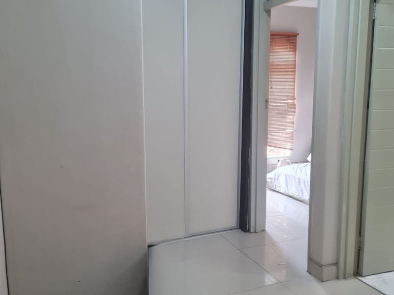 A clean hallway featuring tiled flooring and a built-in sliding door cupboard, providing functional storage space and access to adjacent rooms.