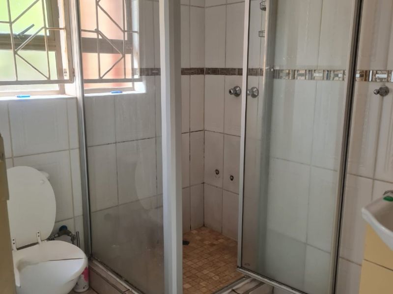 A functional bathroom featuring a shower enclosure, toilet, and vanity cabinet, with tiled finishes throughout. The space would benefit from cosmetic updates.
