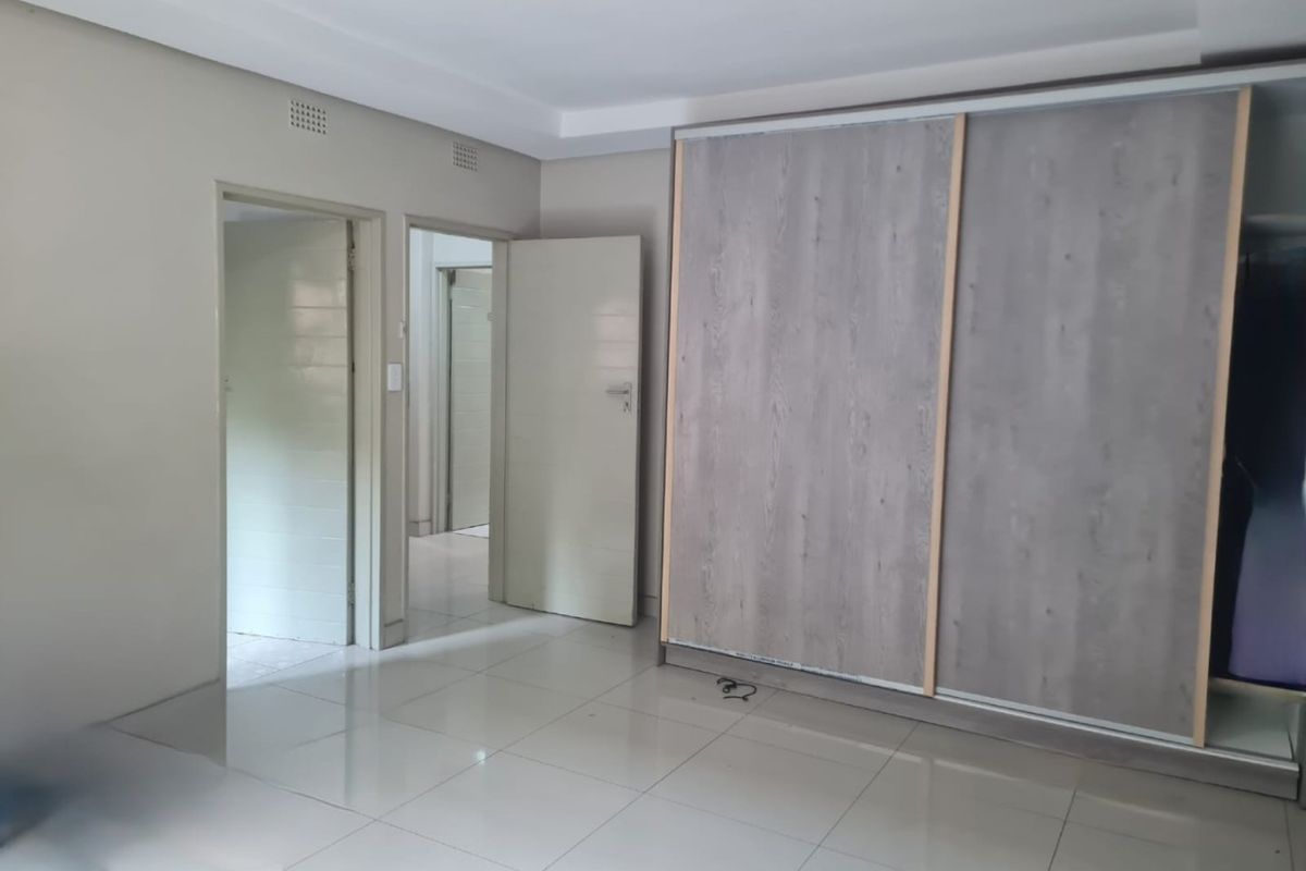 A spacious, empty bedroom featuring modern tiled flooring, a large built-in wardrobe with wood-grain sliding doors, and neutral wall finishes.