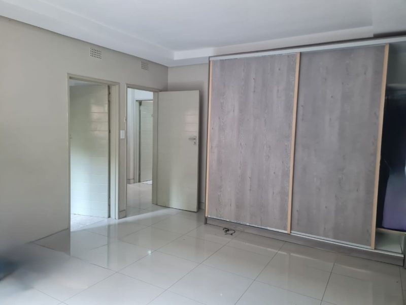 A spacious, empty bedroom featuring modern tiled flooring, a large built-in wardrobe with wood-grain sliding doors, and neutral wall finishes.
