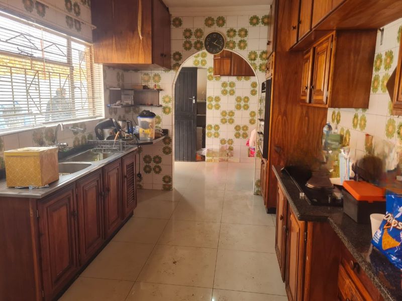 A dated kitchen featuring traditional wooden cabinetry, tiled walls, and a double basin sink, offering significant potential for a modern renovation.