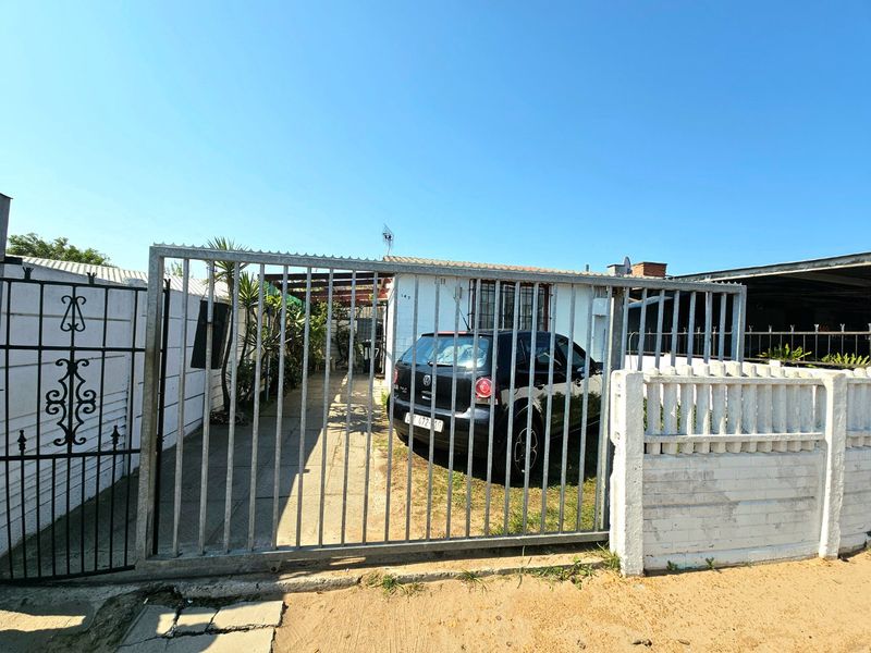 Front exterior view of the property featuring a metal sliding gate, concrete driveway, and perimeter boundary wall with security bars.