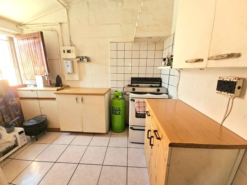 A dated kitchen featuring tiled flooring, tiled splashbacks, built-in cabinetry, and a gas stove, requiring significant cosmetic updates and modernization.