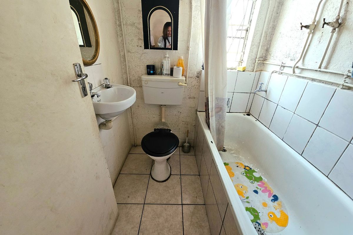 A compact bathroom featuring a wall-mounted basin, toilet, and bathtub with tiled finishes, currently requiring significant maintenance and cosmetic updates.