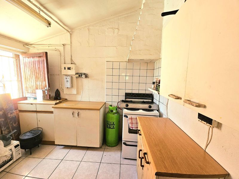 A dated kitchen featuring tiled flooring, built-in cabinetry, and a gas stove, requiring significant modernization and cosmetic updates to improve functionality and aesthetic appeal.
