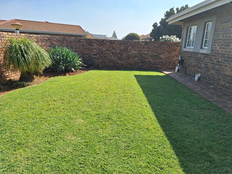 A private rear garden featuring a well-maintained lawn, paved walkway, and secure brick boundary wall, providing a clean and functional outdoor space.
