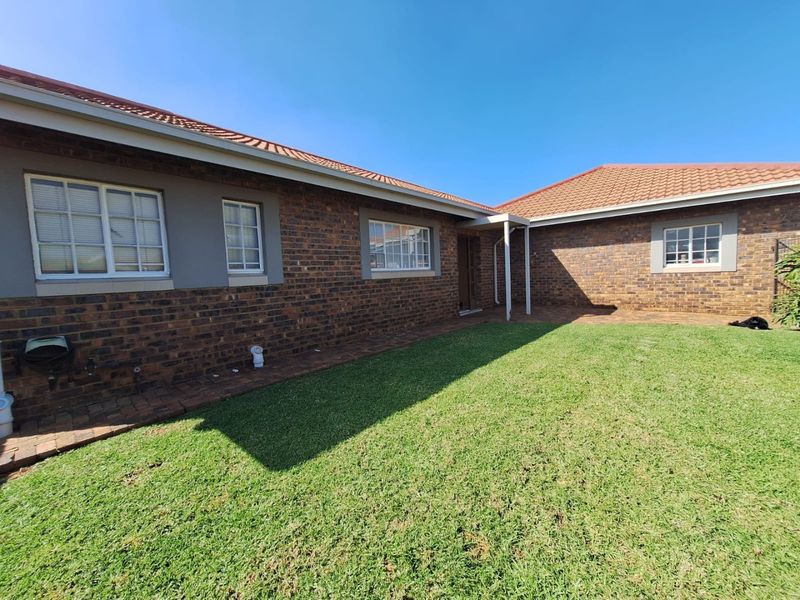 A well-maintained rear exterior view of a face brick townhouse featuring a tiled roof, paved patio area, and a neat lawn.