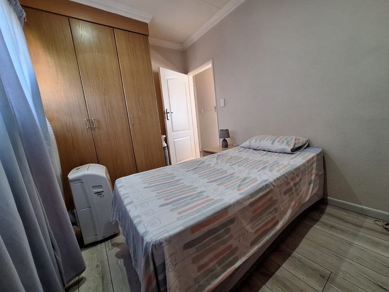 A functional bedroom featuring built-in wooden cupboards, tiled flooring, and neutral wall finishes, providing a practical and comfortable living space.