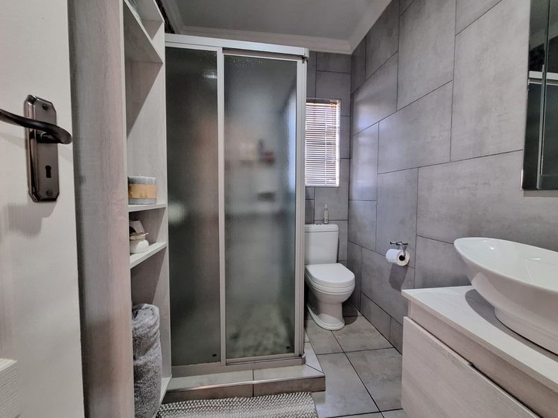 Modern bathroom featuring a glass shower enclosure, vessel sink with vanity cabinet, and contemporary grey wall tiling.