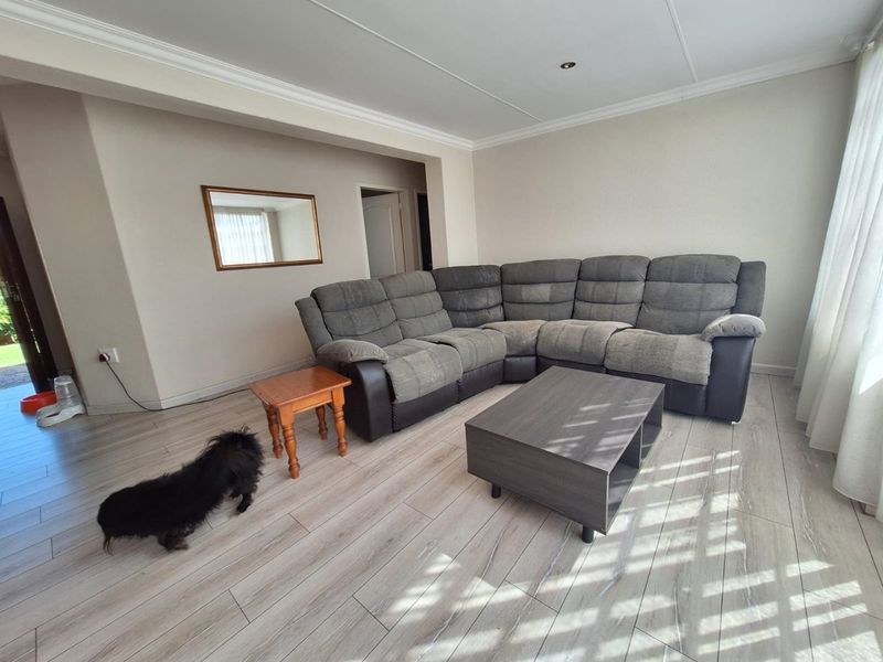 A bright living room featuring modern light-toned laminate flooring, neutral wall finishes, and recessed ceiling lighting, providing a clean and functional living space.