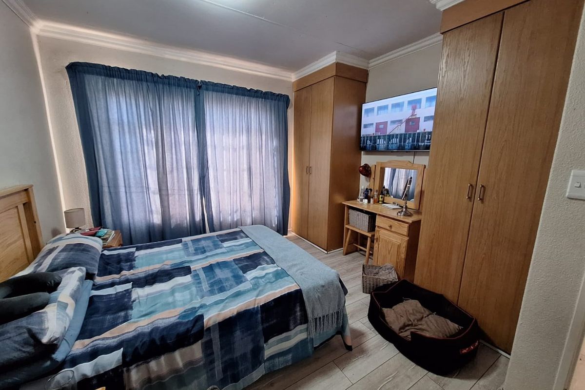 A functional bedroom featuring built-in wooden cupboards, laminate flooring, and coved ceiling details, providing ample storage and a comfortable living space.