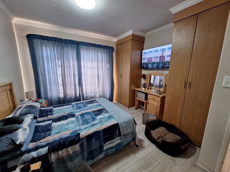 A functional bedroom featuring built-in wooden cupboards, laminate flooring, and coved ceiling details, providing ample storage and a comfortable living space.