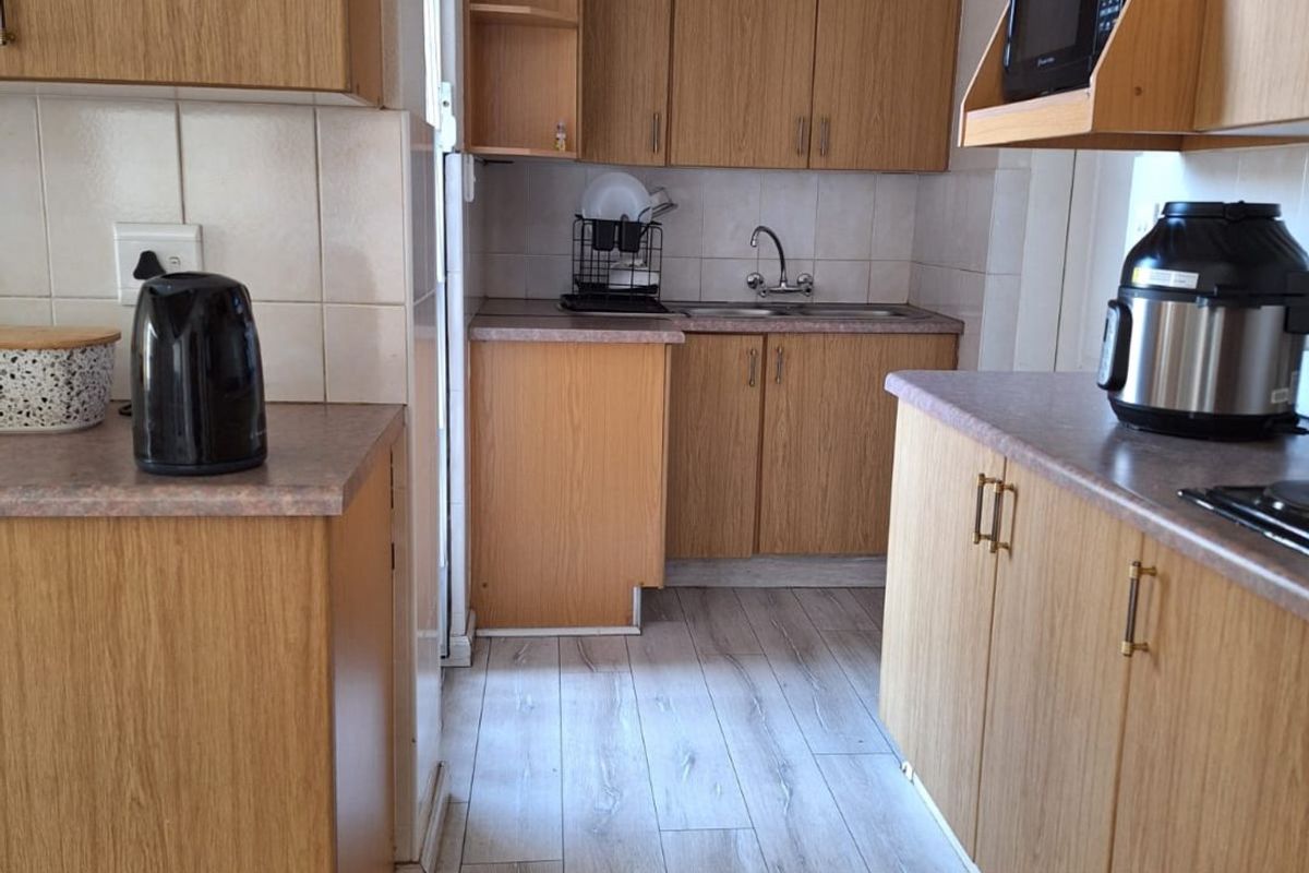 A functional kitchen featuring wood-look laminate cabinetry, tiled backsplash, and durable countertops, offering a practical layout for daily meal preparation.