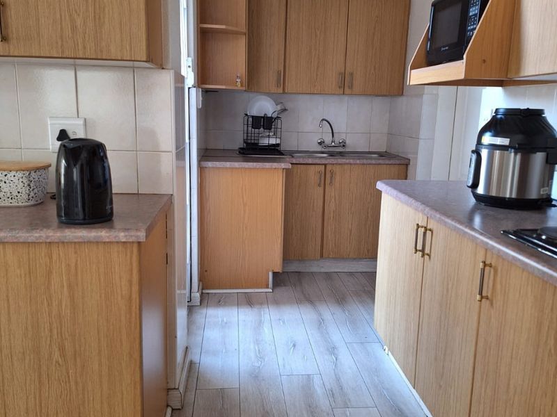 A functional kitchen featuring wood-look laminate cabinetry, tiled backsplash, and durable countertops, offering a practical layout for daily meal preparation.